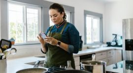 Seorang wanita tengah berinteraksi dengan perangkat rumah pintar, menunjukkan integrasi teknologi yang mulus dalam aktivitas sehari-hari di dalam rumah modern. Gambar ini merefleksikan kenyamanan dan efisiensi yang ditawarkan oleh perangkat cerdas masa kini.