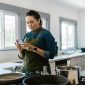 Seorang wanita tengah berinteraksi dengan perangkat rumah pintar, menunjukkan integrasi teknologi yang mulus dalam aktivitas sehari-hari di dalam rumah modern. Gambar ini merefleksikan kenyamanan dan efisiensi yang ditawarkan oleh perangkat cerdas masa kini.