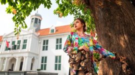Model mengenakan busana perpaduan batik modern dengan siluet futuristik, menampilkan keindahan warisan budaya Indonesia yang diinterpretasikan ulang secara kontemporer. Kombinasi warna cerah dan detail inovatif memancarkan aura kepercayaan diri yang siap menyambut masa depan fashion.