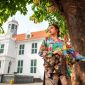 Model mengenakan busana perpaduan batik modern dengan siluet futuristik, menampilkan keindahan warisan budaya Indonesia yang diinterpretasikan ulang secara kontemporer. Kombinasi warna cerah dan detail inovatif memancarkan aura kepercayaan diri yang siap menyambut masa depan fashion.