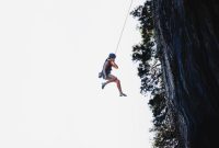 Seorang wanita terlihat tenang menghadapi terpaan angin kencang di puncak gunung, merepresentasikan ketangguhan mental yang diperlukan untuk menghadapi ketidakpastian hidup. Gambar ini menunjukkan bahwa dengan pola pikir yang tepat, setiap individu mampu menghadapi tantangan dengan ketenangan dan kekuatan batin.