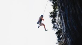 Seorang wanita terlihat tenang menghadapi terpaan angin kencang di puncak gunung, merepresentasikan ketangguhan mental yang diperlukan untuk menghadapi ketidakpastian hidup. Gambar ini menunjukkan bahwa dengan pola pikir yang tepat, setiap individu mampu menghadapi tantangan dengan ketenangan dan kekuatan batin.