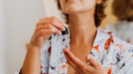 Seorang wanita tengah mengaplikasikan serum wajah di depan cermin, menggambarkan komitmen terhadap rutinitas perawatan kulit harian. Ini merupakan representasi visual dari dedikasi terhadap kesehatan kulit yang memancarkan kilau alami, melampaui sekadar produk kosmetik.