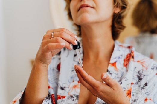 Seorang wanita tengah mengaplikasikan serum wajah di depan cermin, menggambarkan komitmen terhadap rutinitas perawatan kulit harian. Ini merupakan representasi visual dari dedikasi terhadap kesehatan kulit yang memancarkan kilau alami, melampaui sekadar produk kosmetik.