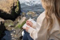 Seorang wanita tersenyum damai sambil menulis di jurnal, mencerminkan momen refleksi diri dan penemuan kebahagiaan di tengah alam yang menenangkan. Kegiatan menulis jurnal dapat menjadi salah satu ritual penting untuk memupuk kebahagiaan dan mengidentifikasi nilai-nilai hidup yang sesungguhnya.