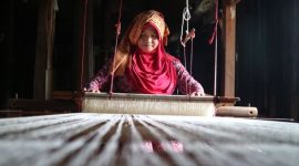 Model mengenakan busana yang memadukan tenun ikat tradisional Indonesia dengan desain kontemporer, merefleksikan tren mode 2026 yang mengedepankan keberlanjutan dan identitas lokal. Pilihan material ramah lingkungan dan sentuhan estetika retro menambah dimensi baru pada koleksi yang relevan untuk gaya hidup modern.