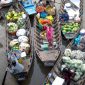 Pemandangan ramai aktivitas jual beli di pasar terapung, menampilkan perahu-perahu kecil penuh dengan aneka dagangan hasil bumi dan kerajinan tangan, berinteraksi langsung dengan pembeli di atas sungai. Suasana pagi yang cerah menambah keindahan interaksi budaya yang telah berlangsung turun-temurun ini.