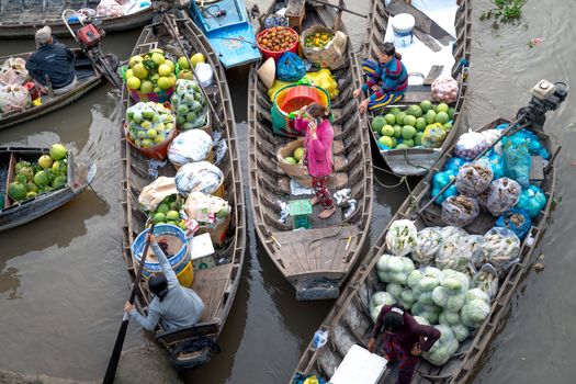 Pemandangan ramai aktivitas jual beli di pasar terapung, menampilkan perahu-perahu kecil penuh dengan aneka dagangan hasil bumi dan kerajinan tangan, berinteraksi langsung dengan pembeli di atas sungai. Suasana pagi yang cerah menambah keindahan interaksi budaya yang telah berlangsung turun-temurun ini.