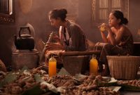 Seorang wanita Banjar sedang meracik ramuan obat tradisional Pilah, menunjukkan bahan-bahan alami seperti akar-akaran dan rempah yang masih mentah, sebuah praktik turun-temurun yang sarat makna. Proses ini menggambarkan dedikasi tinggi dalam melestarikan kearifan lokal pengobatan herbal yang telah ada sejak lama.