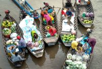 Pemandangan pasar terapung yang hidup di Kalimantan, menampilkan para pedagang berinteraksi dari atas jukung mereka yang penuh dengan aneka hasil bumi segar, sebuah tradisi yang terus lestari.