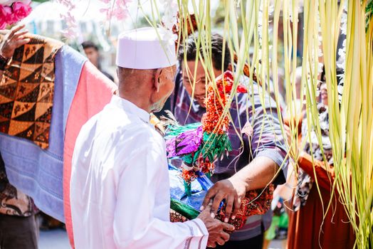 Seorang ibu mengayunkan bayinya dalam buaian kain sasirangan penuh warna selama upacara Baayun Mulud, tradisi khas masyarakat Banjar di Kalimantan Selatan untuk memperingati Maulid Nabi Muhammad SAW. Pemandangan ini mencerminkan kehangatan keluarga dan kekayaan budaya yang diwariskan secara turun-temurun.