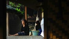 Seorang warga Dayak Meratus berdiri di depan rumah adat mereka yang kokoh, melambangkan kuatnya akar tradisi dan kebersamaan dalam menghadapi tantangan zaman. Bangunan ini tidak hanya tempat tinggal, tetapi juga pusat aktivitas sosial dan spiritual komunitas.